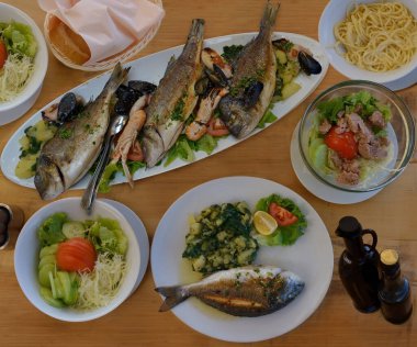 Appetizing seafood as lunch .Langoustines , red mullet, sea bass grilled with lemon, potato  ,shellfish ,pasta ,bread, sauce and salad on the table in the restaurant , Croatia