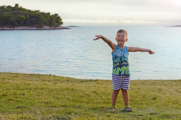 快乐的男孩微笑着 傍晚时分 他的胳膊伸展在海滩上 快乐的生活方式童年的概念 — 图库照片