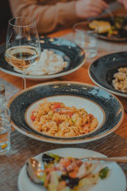 Italian restaurant table with dinner of pasta salad and a glass of wine. Pleasant atmosphere