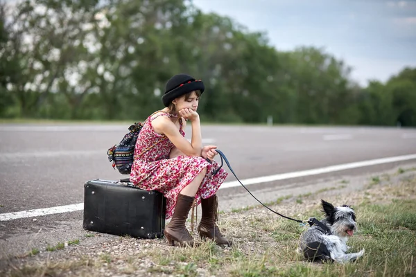 一个孤独的女孩 带着狗和手提箱站在路上 — 图库照片