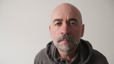 Close up portrait of serious old man with grey beard in the glasses looking astonishment to the camera.