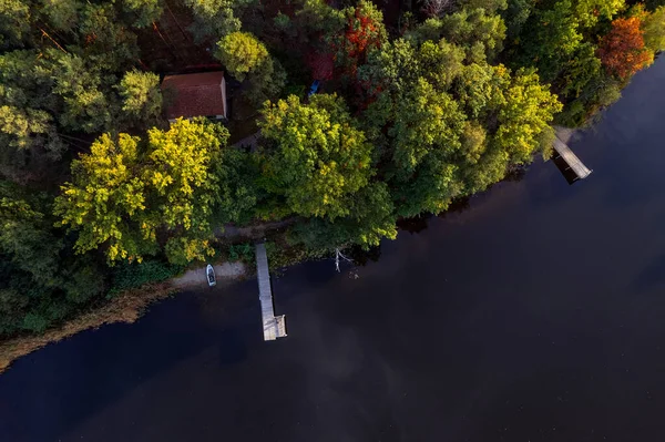 A drone flies over a huge blue lake with a wooden pier among the forests on a cloudless autumn day at dawn.