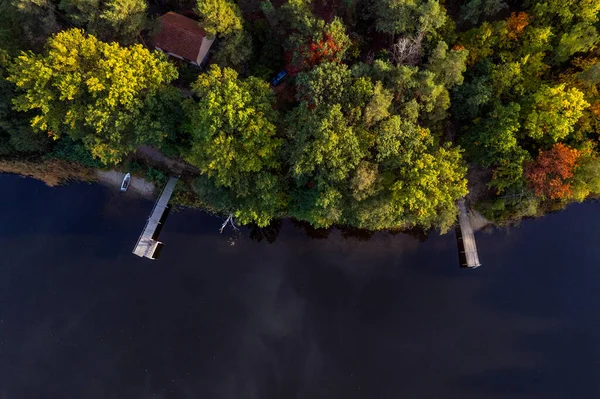 A drone flies over a huge blue lake with a wooden pier among the forests on a cloudless autumn day at dawn.