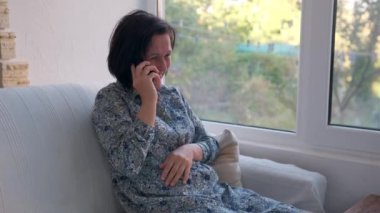 Zarif bir yetişkin kadın verandada oturuyor ve telefonuyla konuşuyor.