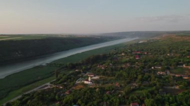 İnsansız hava araçları Dinyester nehrinin kıyısında beyaz bir kilisesi olan bir peri masalı köyünün üzerinde uçuyor. Moldova Cumhuriyeti.