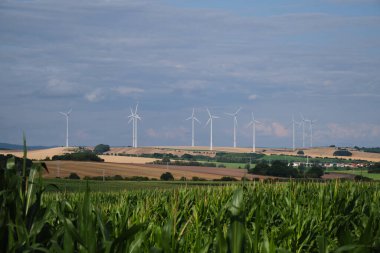 Yeşil mısır tarlası ve rüzgar gücü türbini beyaz bulutlu mavi gökyüzüne karşı. Yenilenebilir enerji kaynağı. Güçlü ve ekolojik enerji kavramı