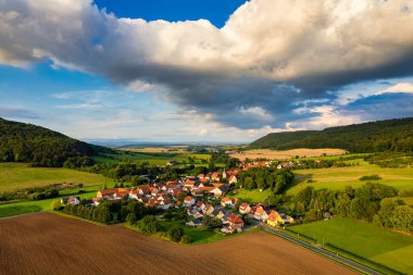 Büyüleyici Alman köyü, gür bir vadi boyunca yayılıyor, canlı çatıları ile mavi gökyüzünün altında, tüylü bulutlarla süslenmiş manzarayı noktalıyor. Doğa her yönde gelişir. Almanya.