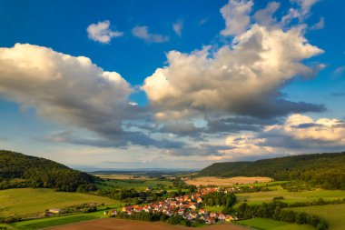Büyüleyici Alman köyü, gür bir vadi boyunca yayılıyor, canlı çatıları ile mavi gökyüzünün altında, tüylü bulutlarla süslenmiş manzarayı noktalıyor. Doğa her yönde gelişir. Almanya.
