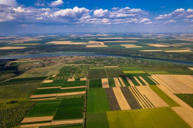 Nefes kesen bir hava görüntüsü canlı yeşil tarlaları ve berrak mavi gökyüzünün altında akan bir nehri yakalar.