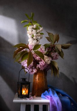 Güzel, sakin bir bahar çiçek aranjmanı narin pembe çiçekler ve büyüleyici bir fener sergiliyor.