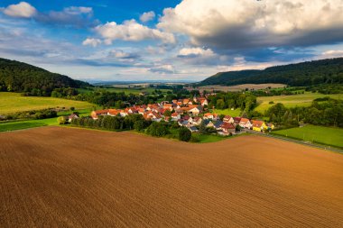 Büyüleyici Alman köyü, gür bir vadi boyunca yayılıyor, canlı çatıları ile mavi gökyüzünün altında, tüylü bulutlarla süslenmiş manzarayı noktalıyor. Doğa her yönde gelişir. Almanya.