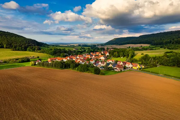 Büyüleyici Alman köyü, gür bir vadi boyunca yayılıyor, canlı çatıları ile mavi gökyüzünün altında, tüylü bulutlarla süslenmiş manzarayı noktalıyor. Doğa her yönde gelişir. Almanya.