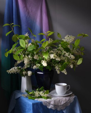 Sakin bir yaşam kompozisyonu açık bir kitap, narin bir çay fincanı ve canlı, gür bir çiçek aranjmanı sergiliyor.