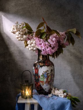 Güzel, sakin bir bahar çiçek aranjmanı narin pembe çiçekler ve büyüleyici bir fener sergiliyor.