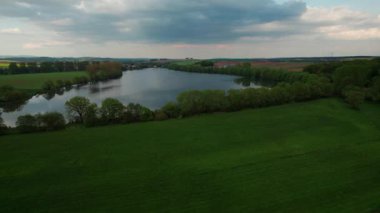 Tarlalarla çevrili samimi bir Alman köyünün yakınındaki gölün üzerinde büyüleyici bir günbatımı. Kuş bakışı görüş. Almanya.