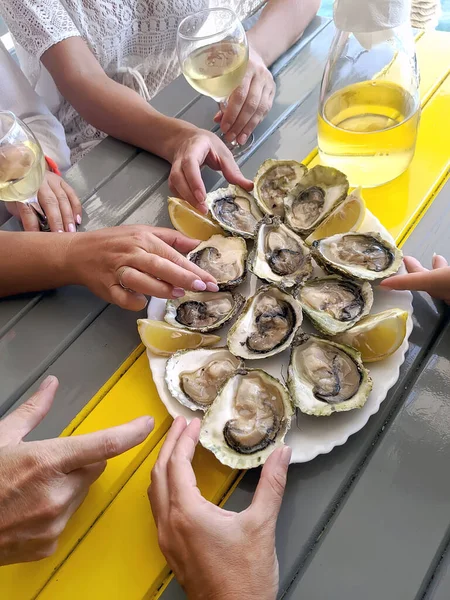 A group of friends are tasting oysters and white wine in a restaurant on the sea coast, a concept for a gastronomic tour