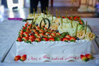 Pastanın üzerinde çilek ve beyaz güller. Kare pastadaki sarı mumlar. 70 yaşında. .