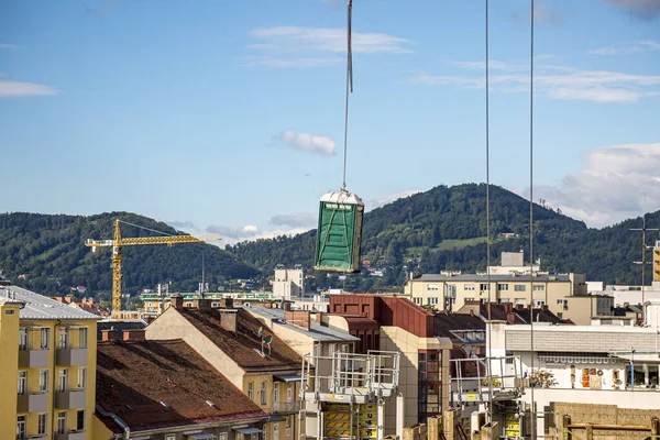 Crane lifted a chemical toilet at a construction site against a blue sky in Graz, Austria.