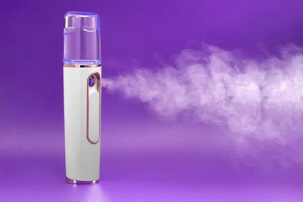 stock image Front view of steam from portable humidifier on purple background. Beauty treatment of face in beauty center.