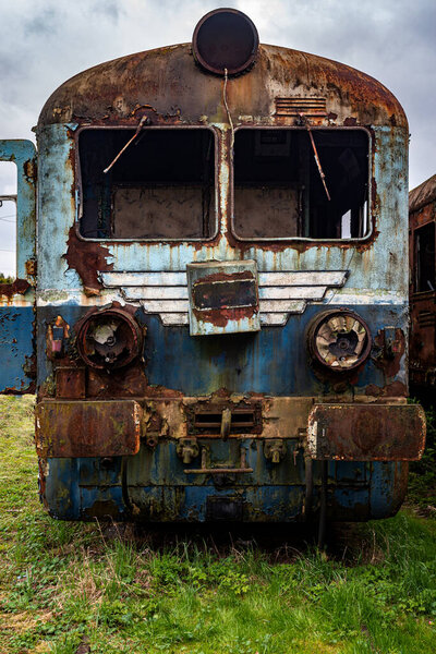 Old rusty electric multiple unit train decommissioned and abandoned on railway siding on green grassy field 