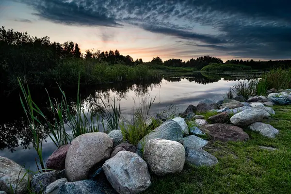 空と雲の美しい湖の上の美しい夕日の風景景は 前景に岩と石で水に反映されています ロイヤリティフリーのストック画像