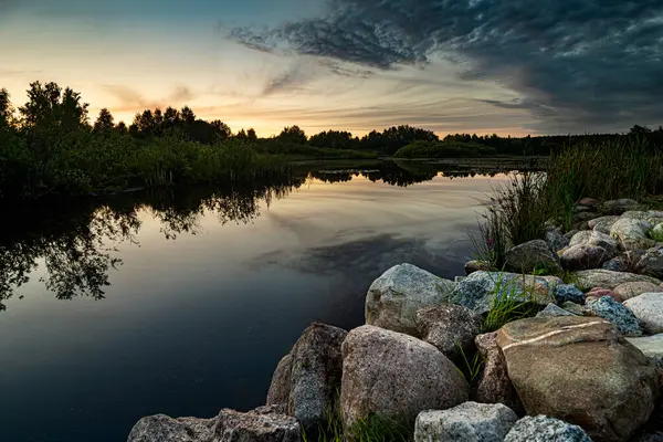 空と雲の美しい湖の上の美しい夕日の風景景は 前景に岩と石で水に反映されています ロイヤリティフリーのストック写真