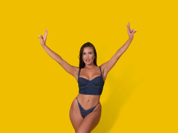 穿着紧身胸衣和紧身裤的性感女性模特儿 带着黄色背景高举双臂的V字形手势 图库图片