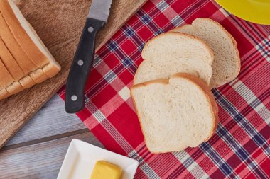 Jamaika bandanasına üç dilim sert hamur ekmeği, sarı tabak, kesim tahtası, bıçak ve tereyağı.