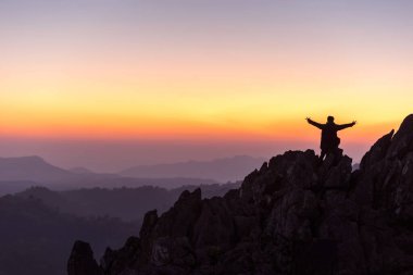 Gün batımında kolları havada bir uçurumun tepesinde duran bir adamın silüeti başarıyı kutluyor.