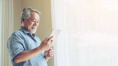 Akıllı telefon kullanan yaşlı bir erkek, gülümsüyor. Yatak odasında mutlu hissediyor. Son sınıf yaşam tarzı konsepti.