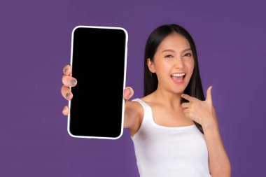 Beautiful Asian brunette woman cute girl in white tank top ,Excited surprised girl showing big smart phone with blank screen , white screen isolated purple background , Mock Up Image