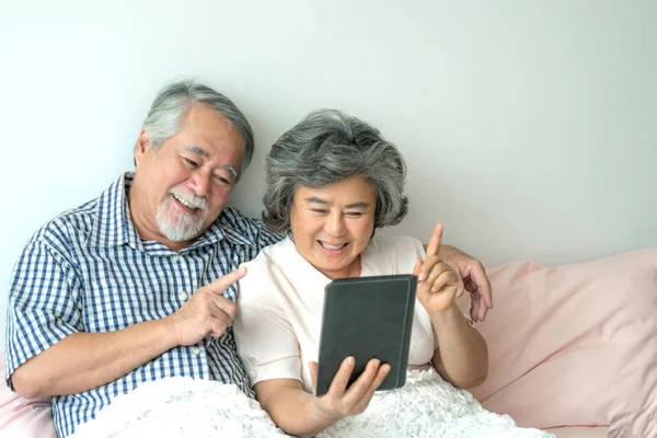 stock image Senior couple using a tablet phone computer face time call to relatives descendant relatives grandchild, smiling feel happy in sofa at home - lifestyle senior concept