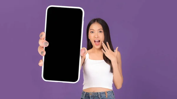 美しいアジアの若い女性の肖像画 黒画面で大きなスマートフォンを示す興奮した驚きの女の子 紫の背景に隔離された白い画面 モックアップ画像 — ストック写真