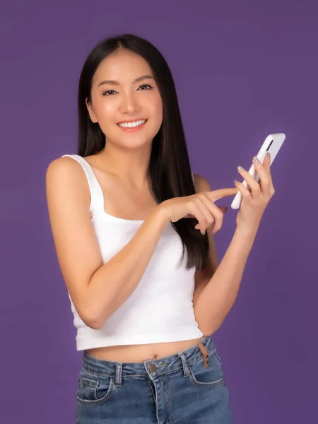 美しいアジアのブルネットの女性かわいい女の子の白いタンクの上に紫色の背景に隔離されたスマートフォンをプレイ 携帯電話はオンラインショッピングを支払うためにオンライン銀行を使用 — ストック写真
