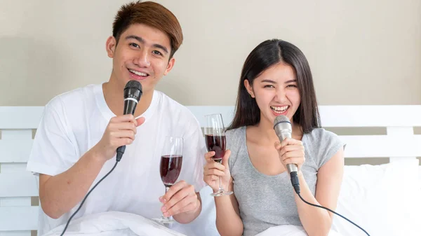 若いアジアのカップルはワインの幸せな保持ガラスを埋めると歌カラオケパーティーを歌うの寝室でお祝い — ストック写真