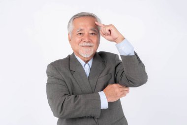 Resmi gri takım elbiseli kıdemli iş adamı, düşünceli bir jest yaparak, bilgeliği, yaratıcılığı ya da stratejik düşünmeyi sembolize ederek, beyaz bir arka planda izole bir şekilde ayakta duruyor.