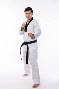 Siyah kuşaklı geleneksel beyaz dobok giyen erkek tekvando sporcusu, beyaz arka planda izole edilmiş beyazlara karşı savaş duruşu sergiliyor.