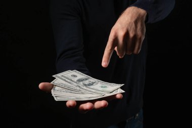 Bir yığın Amerikan doları tutan ve parmakla işaret eden adam, zenginliği, finansal başarıyı, yatırım fırsatlarını, para yönetimini ve siyah bir arkaplanda para kazancını temsil ediyor.