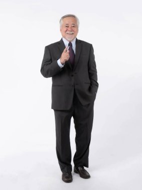 Resmi siyah takım elbiseli kendinden emin kıdemli Asyalı işadamı, gülümseyip ileri işaret ediyor, liderlik, profesyonellik ve başarıyı temsil ediyor, beyaz arka planda tek başına duruyor.