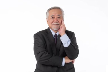 Resmi gri takım elbiseli kıdemli iş adamı, düşünceli bir jest yaparak, bilgeliği, yaratıcılığı ya da stratejik düşünmeyi sembolize ederek, beyaz bir arka planda izole bir şekilde ayakta duruyor.