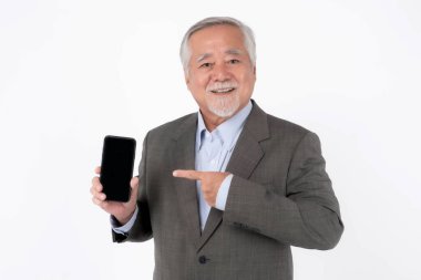 Kıdemli Asyalı Adam Siyah Ekran ile Smartphone 'a gülümsüyor ve işaret ediyor, Resmi Takım Elbise ve Açık Mavi Gömlek Giyiyor, Beyaz Arkaplanda İzole Edilmiş, İş, Teknoloji veya Uygulama Tanıtımları İçin İdeal