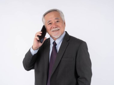 Koyu takım elbiseli gülümseyen Asyalı bir işadamı, akıllı bir telefonla temiz beyaz bir arkaplan karşısında konuşuyor, iş dünyasında modern iletişimi sergiliyor.
