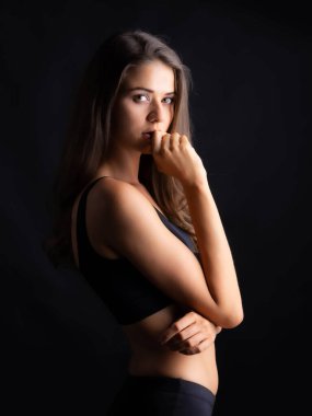 Uzun kahverengi saçlı dalgın genç bir kadın, siyah bir bluz giyiyor, Moody Stüdyolarında Karanlık Bir Arkaplanda Kaybolmuş.