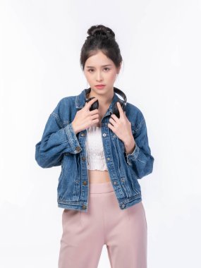 Kot ceketli, kulaklıklı, modaya uygun ve kendinden emin görünen, beyaz bir arka planda izole edilmiş, sıradan bir manken ya da müzik aşığı yaşam tarzı konsepti olan güzel bir kadın.