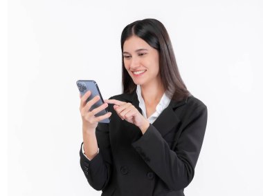 Uzun siyah saçlı, gülümseyen genç iş kadını, siyah ceket giyiyor, akıllı telefonuna bakıyor ve kullanıyor, beyaz arka planda izole edilmiş, iş iletişimi için mobil teknoloji sergiliyor.