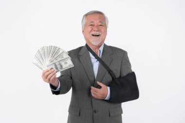 Kolu sakat, parası, sağlık tazminatı ya da sigorta tazminatı ödemesi konsepti olan yaşlı ve emekli bir işadamı, beyaz arka planda izole edilmiş parayla gülümsüyor.