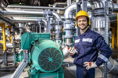 Portrait of smiling caucasian blue collar worker standing by gas fuel engines inside power plant.