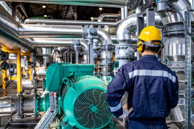 Refinery worker standing by gas fuel engines inside power plant checking production of electricity.