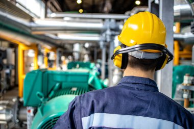 Refinery worker standing by gas fuel engines inside power plant checking production of electricity.