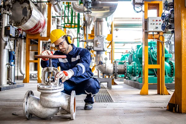 Hardworking industrial technician inspecting high pressure valve inside refinery plant.